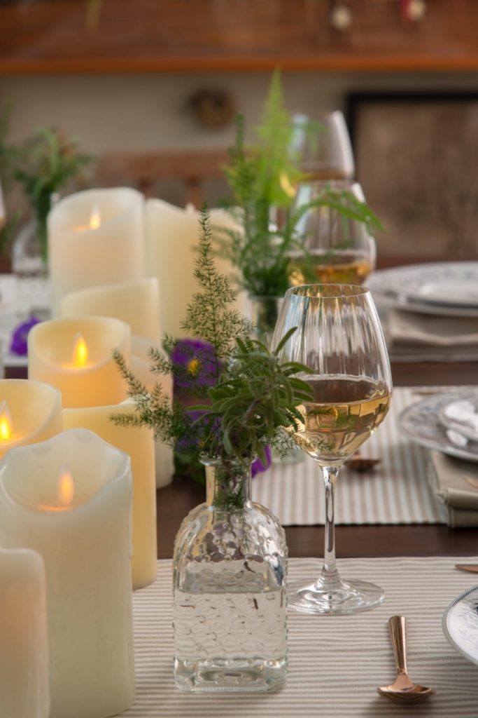 Foto aproximada de um detalhe da mesa: um vidro com arranjo de ramos verdes.