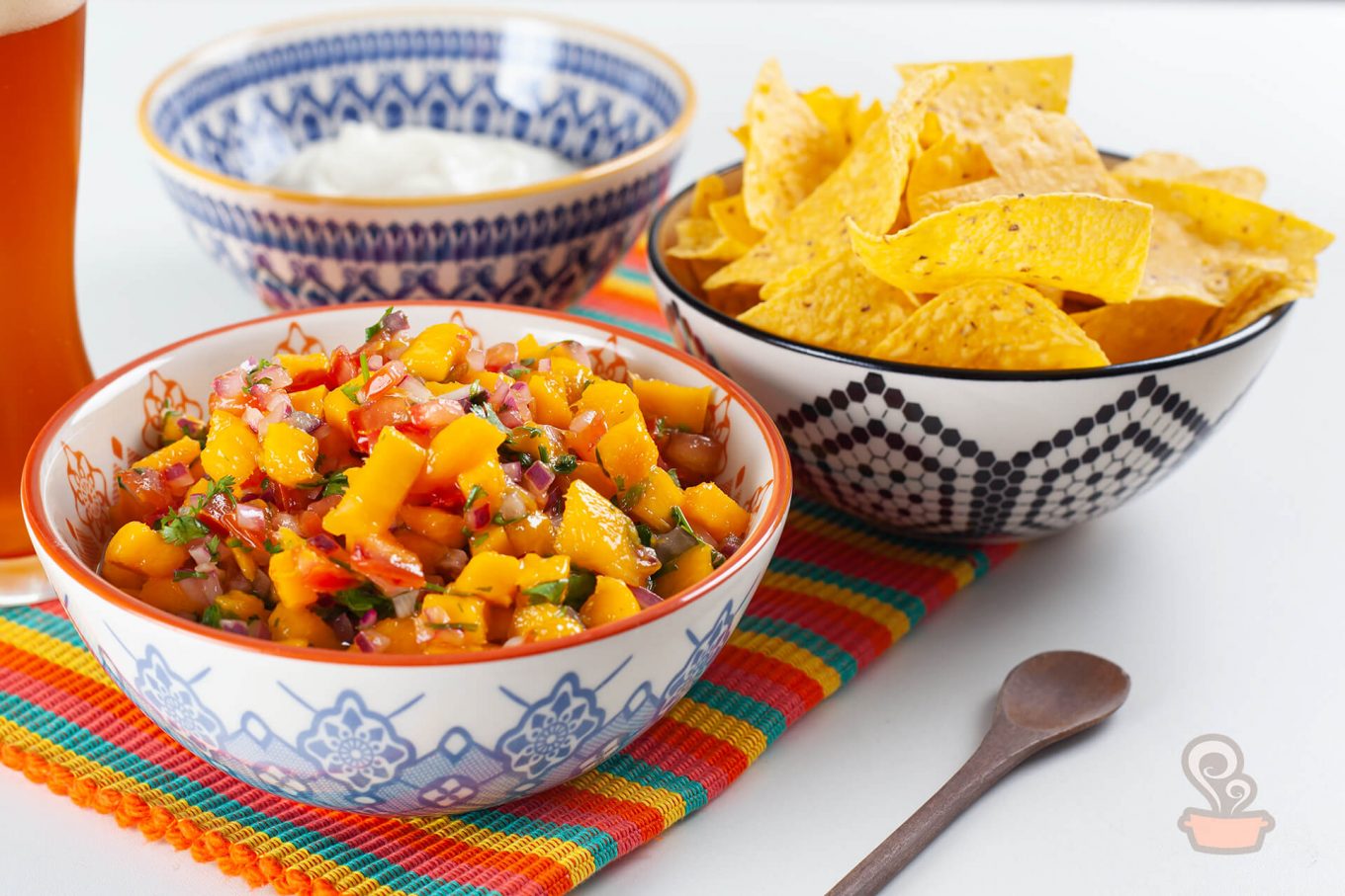 Três tigelas de porcelana. uma com salsa de manga, outra com tortilhas de milhos e a terceira, vazia.