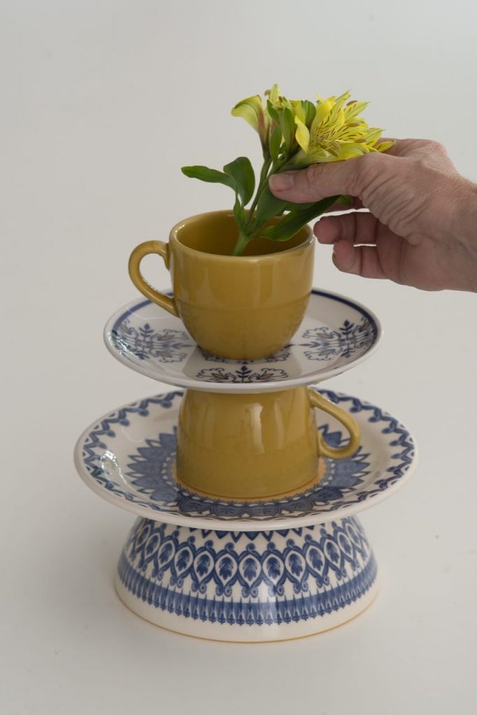 Ramo de flores amarela sendo colocada na xícara que fica no topo do prato de dois andares.