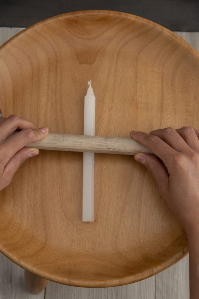 Duas mão seguram o bastão de madeira sobre a vela