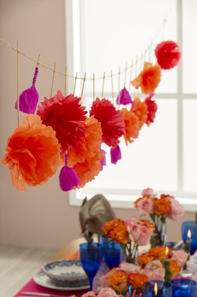 Varal com flores de papel em tons de laranja, vermelho e pink. 