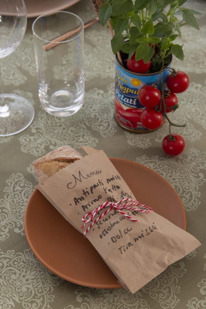 Pão tipo ciabatta dentro de um saquinho de papel pardo, com o menu do almoço italiano escrito a mão