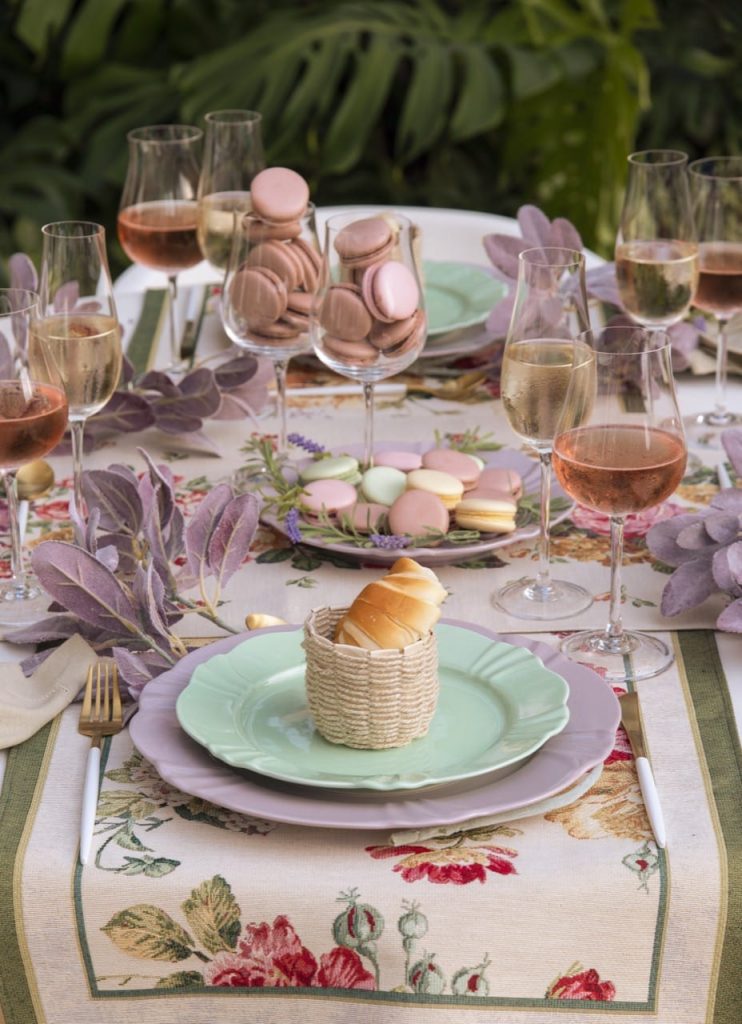 No centro da mesa posta francesa, vemos macarons em um prato e em duas taças de cristal. 