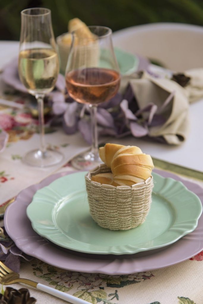 Sobreposição de cestinha de pão, prato de sobremesa em tom de verde, prato raso em tom de lilás. 