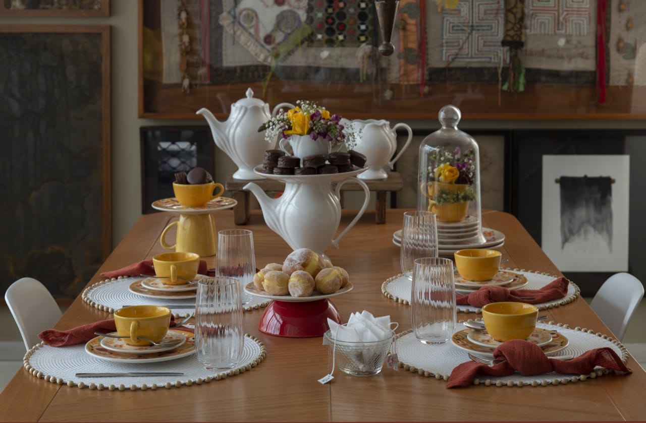 Mesa posta para o chá da tarde com louças em tons de amarelo, laranja e branco. 