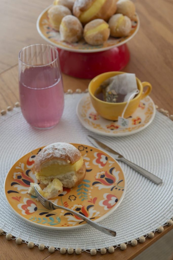 No prato de sobremesa, temos parte de um sonho. Ao lado, xícara com chá e copo com limonada rosa. 