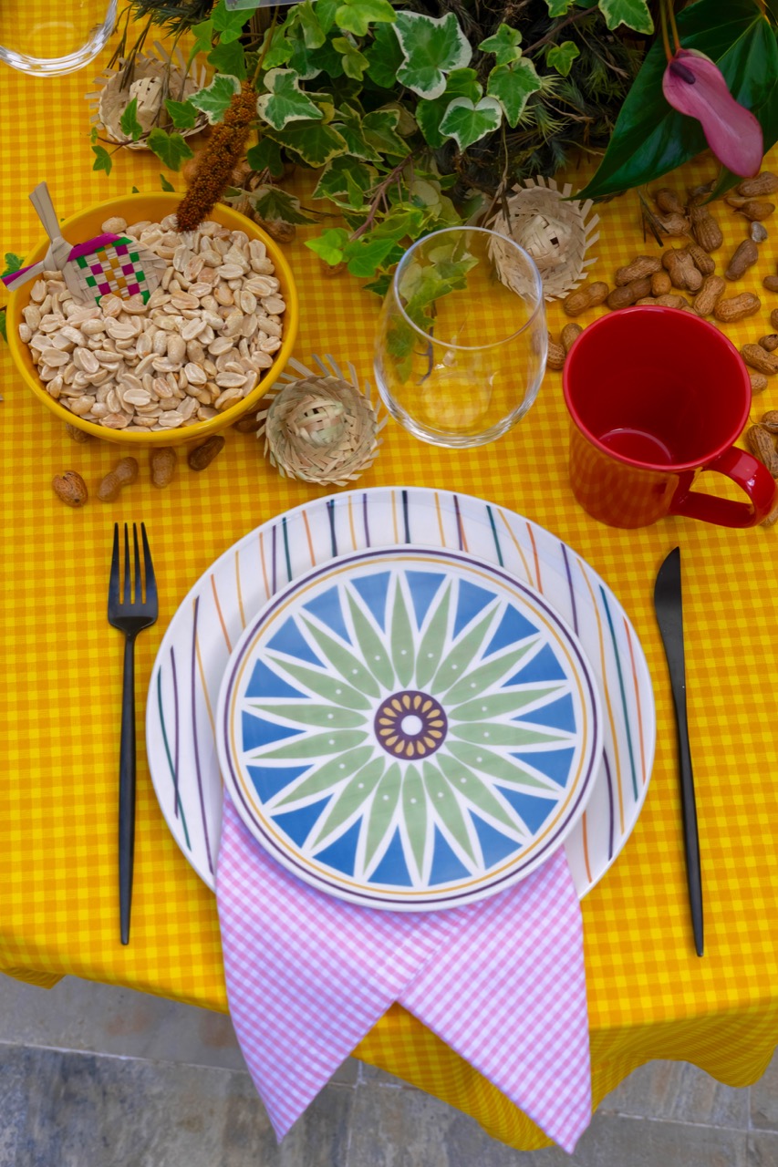 Lugar na mesa posta visto de cima, com pratos estampados e guardanapodobrado em forma de bandeirinha.