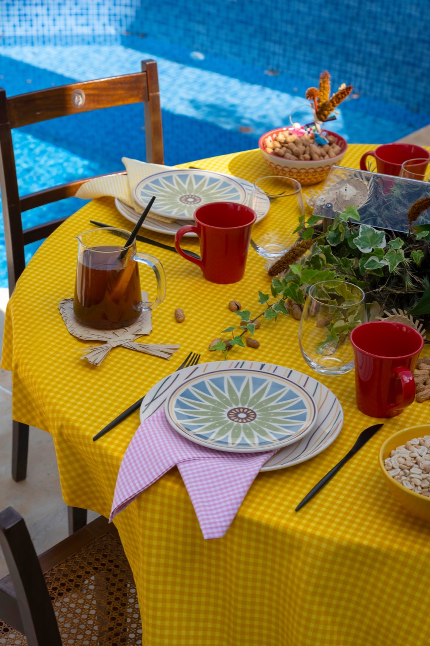 Mesa posta ao ar livre, com toalha amarela e guardanapos em forma de bandeirinha.