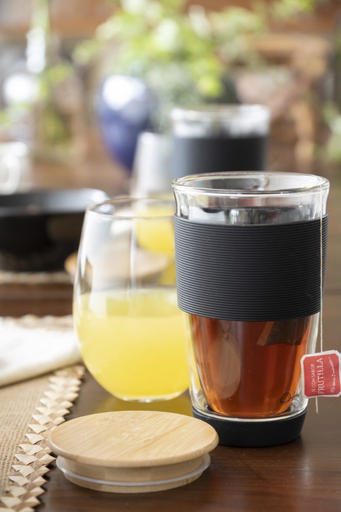 Copo com chá com faixa de borracha preta e tampa de bambu ao lado.