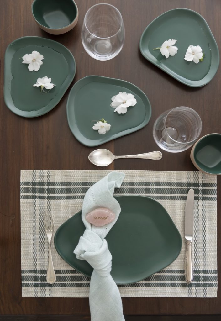Lugar na mesa posta, e três pratos com flores brancas no centro da mesa. 