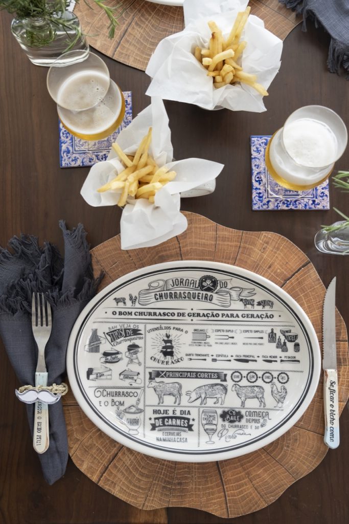 Foto feita de cima mostra lugar na mesa posta com prato oval, estampado em preto. 