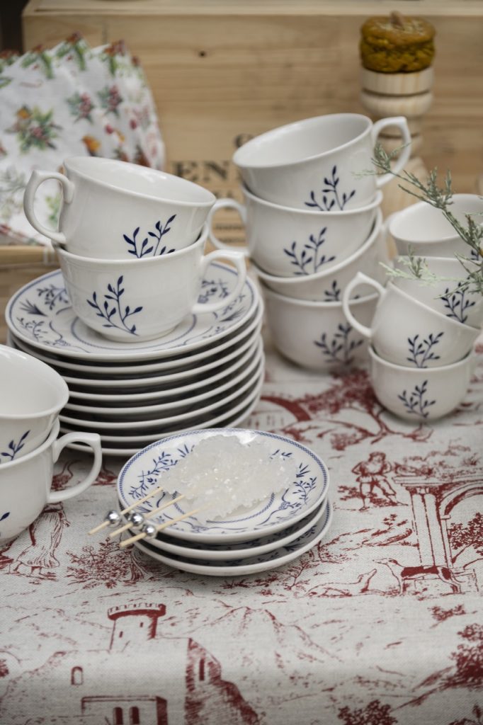 Na mesa de café da manhã  natalina, vemos 12 xícaras, 9 pratos de sobremesa e 3 pires, em pilhas de tamanhos variados. Tudo de porcelana branca com estampa de ramos em azul escuro. 