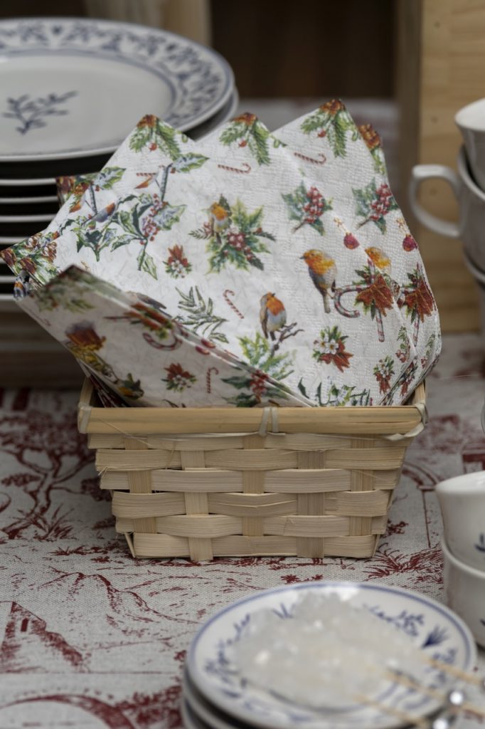 Foto aproximada mostra uma cesta de palha contendo guardanapos de papel com estampa natalina