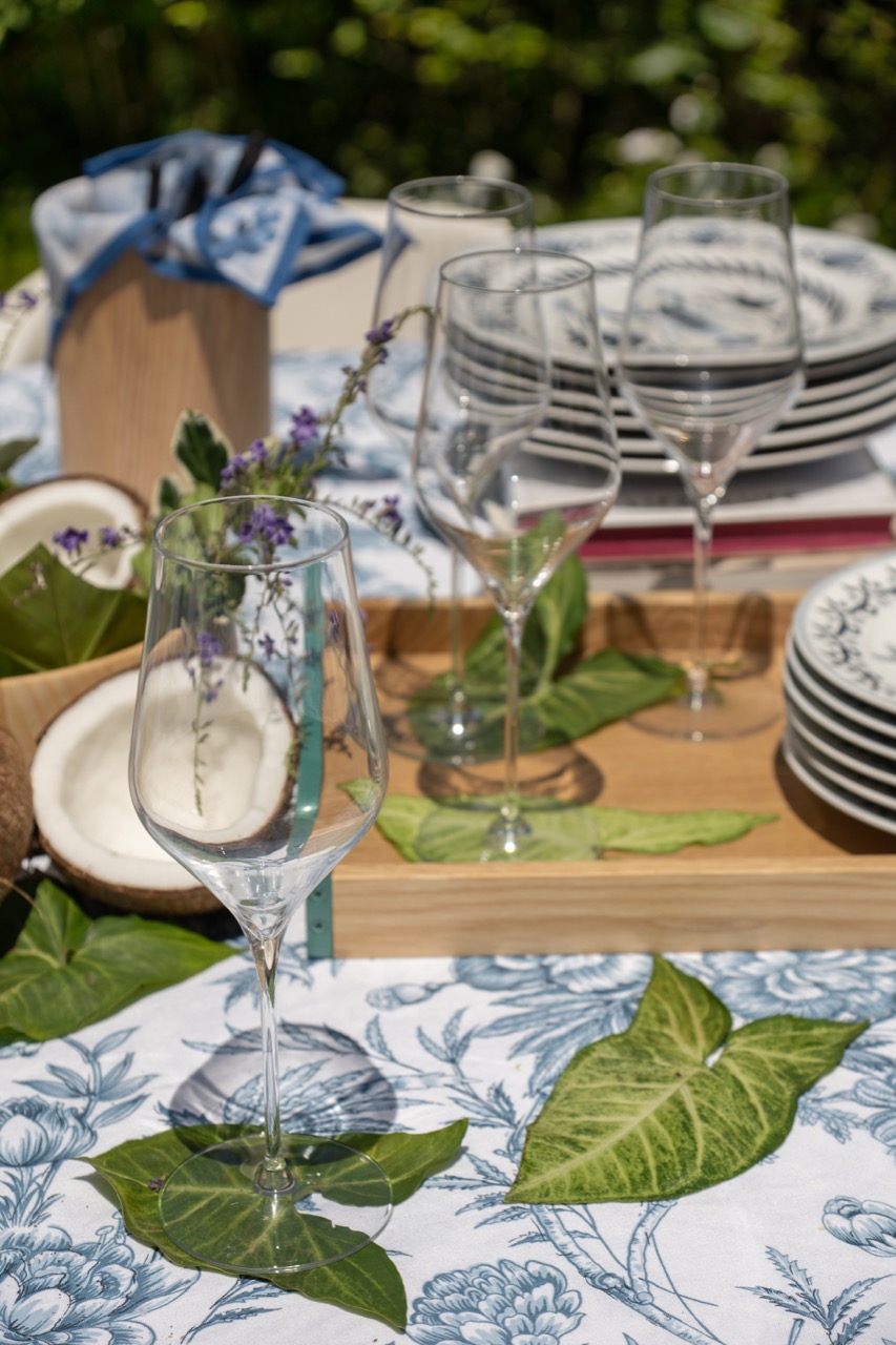 Sobre a mesa de almoço, vemos quatro taças de cristal sobre folhas verdes naturais. 