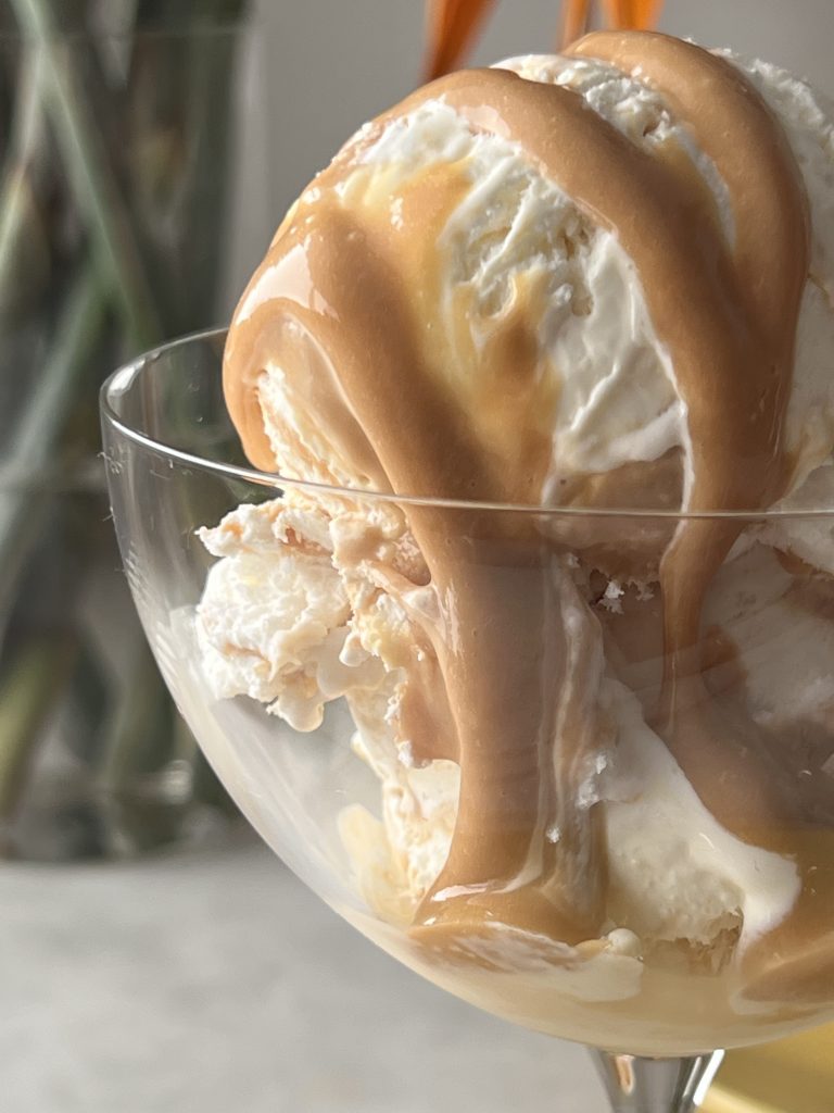 Imagem: sorvete de queijo servido em taça coupe com calda de doce de leite. 