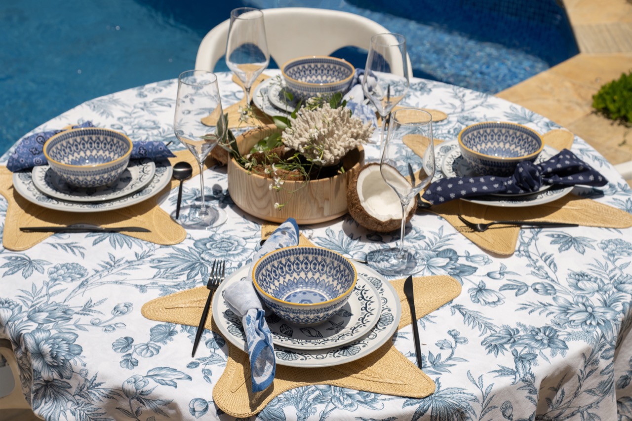 Mesa redonda, à beira da piscina. A toalha, as louças e so guardanapos têm estampas coordenadas em azul e branco.  