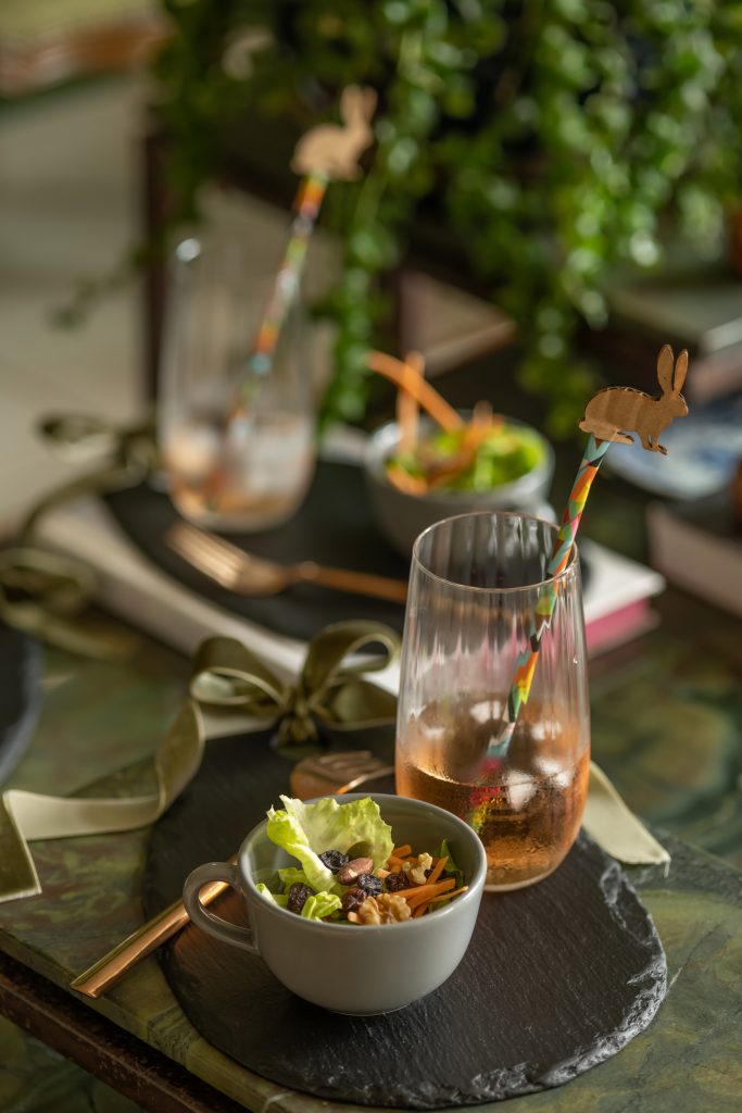 Imagem: tábua preto com xícara de aperitivos e copo ondulado com drink para almoço de Páscoa.