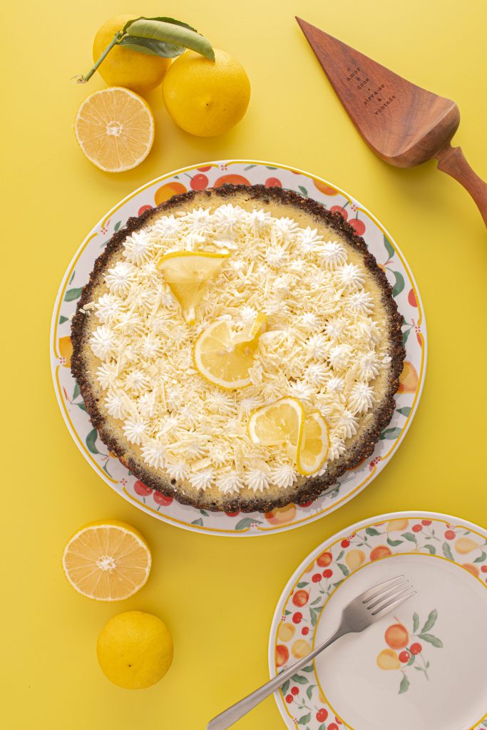 Imagem: torta de limão servida em prato com abas decoradas com frutas. 