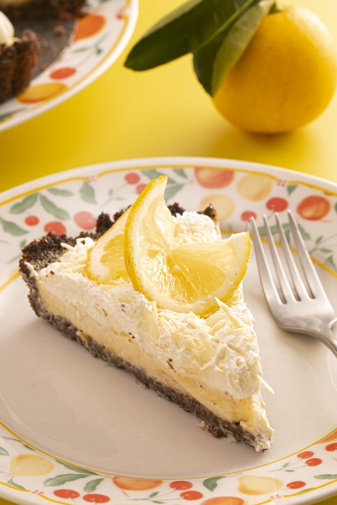 Imagem: fatia de torta de limão servida em prato com abas decoradas com frutas. 