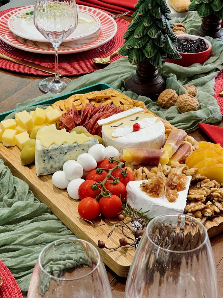 Imagem: tábua de madeira servida com queijos, salames e frutas. O destaque fica para o queijo camembert em formato de papai noel. 