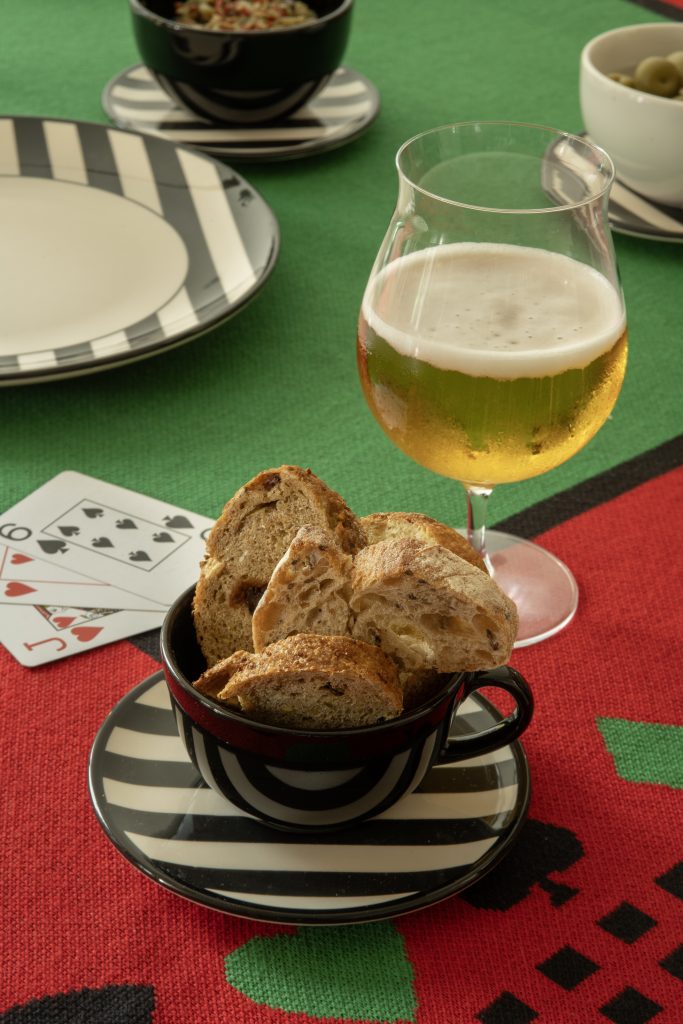 Imagem: mesa com toalha para jogo com pratos de bolinhas e cartas de baralho.