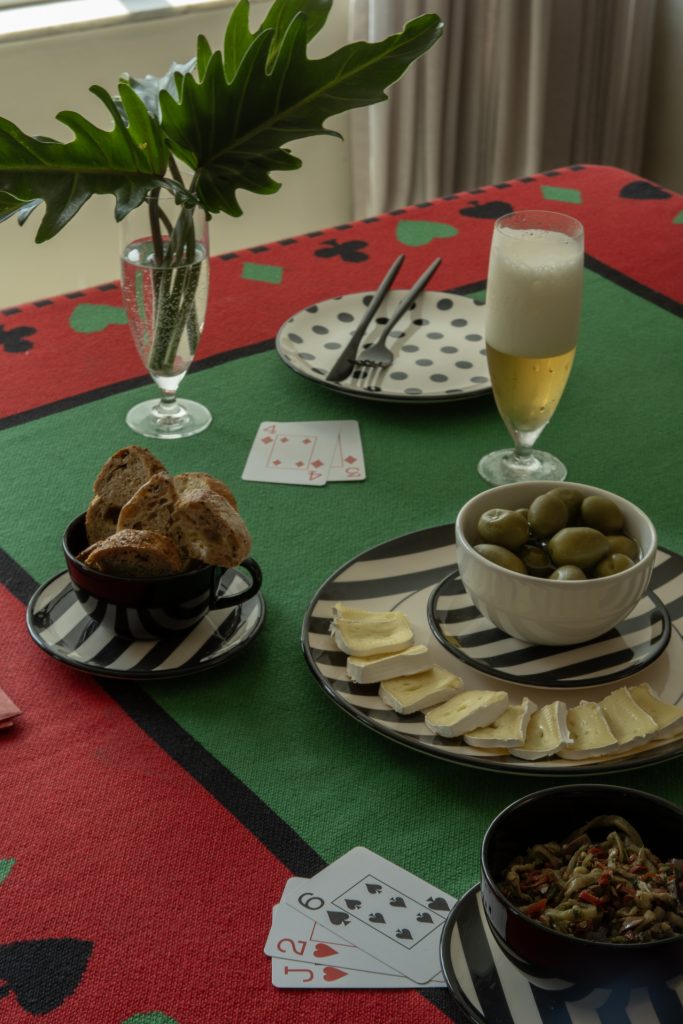 Imagem: mesa com toalha para jogo com pratos de bolinhas e cartas de baralho.