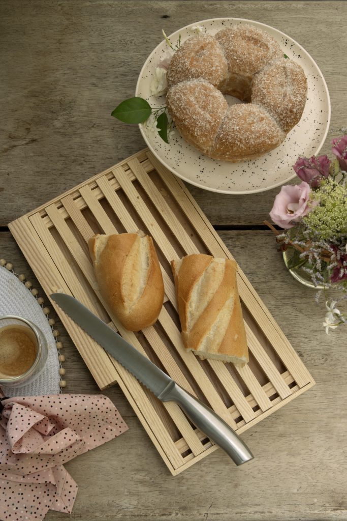 Imagem: pão sobre tábua migalheira e bolo servido em boleira de bolinhas.