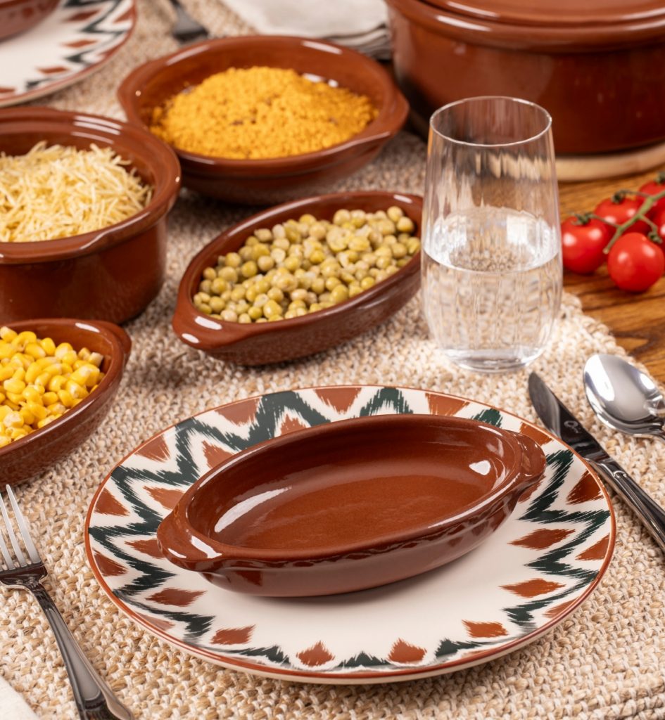 Imagem: Cachorro-quente servido em travessa da linha Feijoada Oxford sobre prato estampado Unni Boho, em mesa posta descontraída.