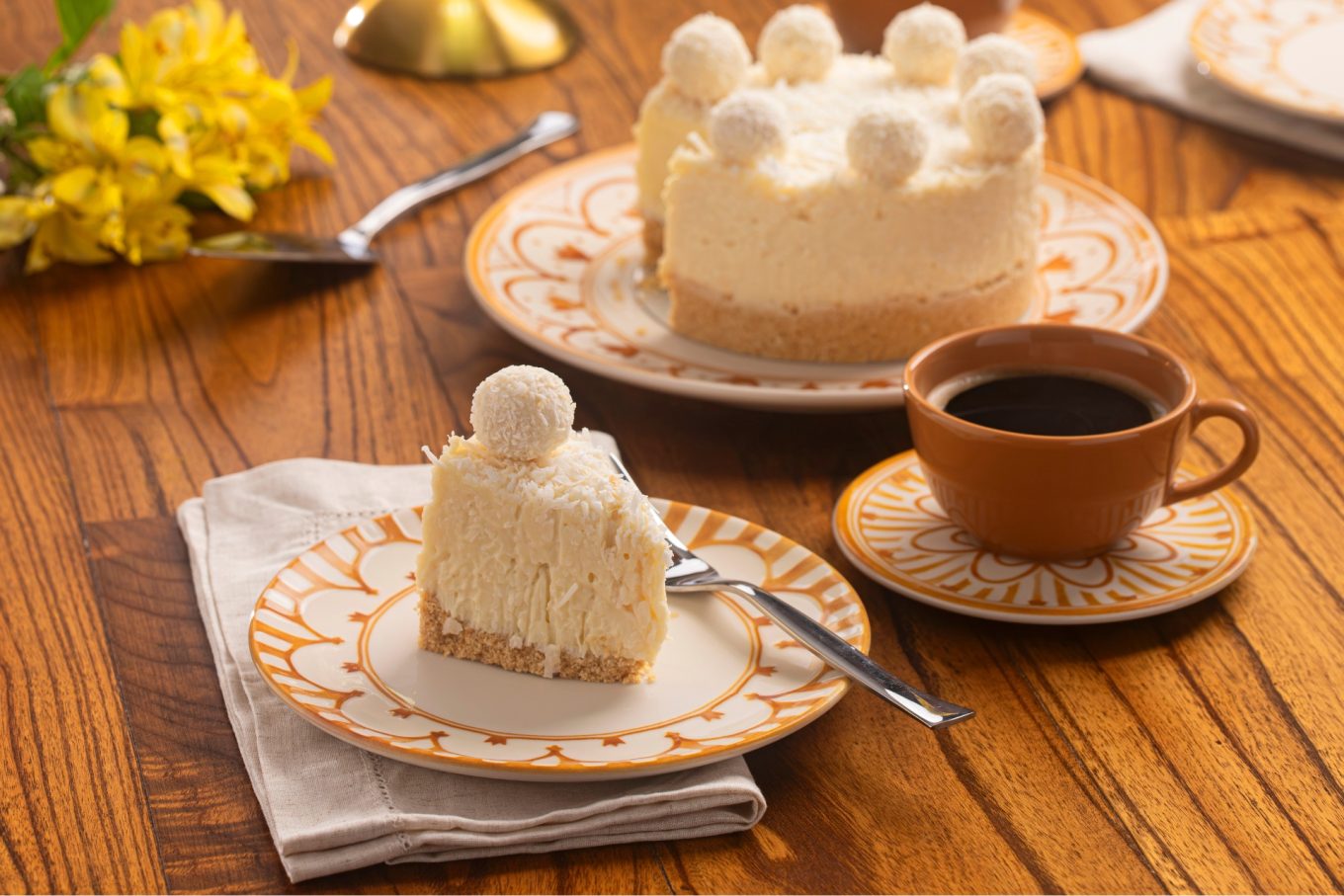 Imagem: pratos com estampa em aquarela amarela servidos com torta de coco e café preto, sobremesa de dia das mães. Linha Unni Nuray da Oxford. 